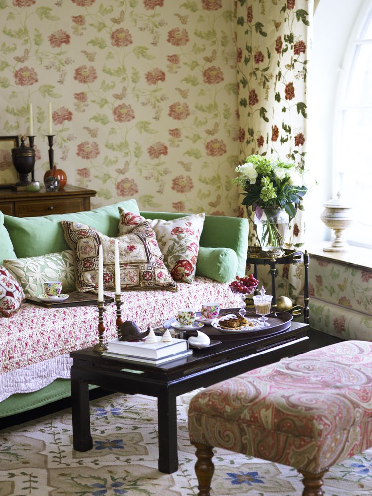 A vintage-inspired room featuring floral rose-patterned wallpaper and a soft seafoam green sofa.