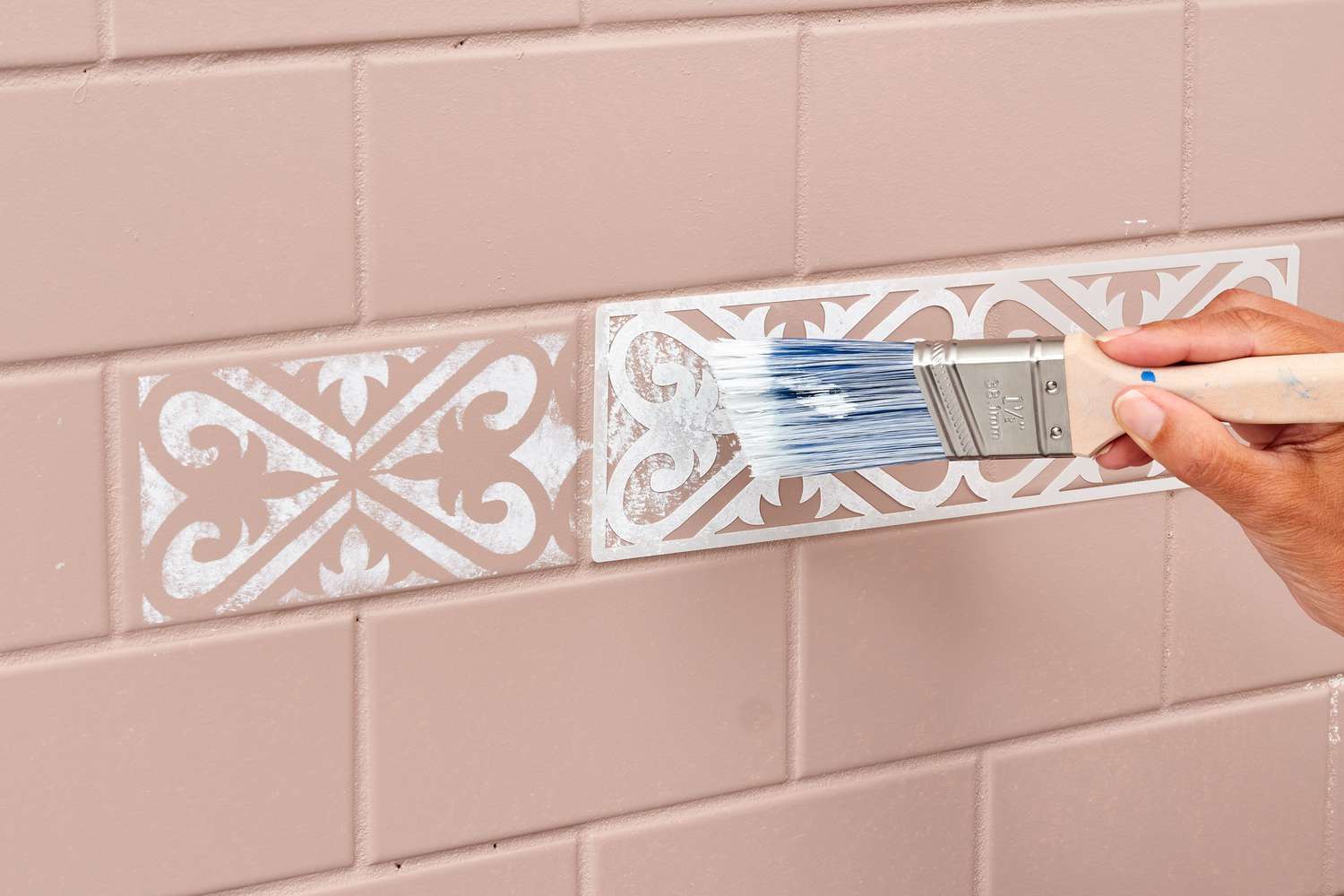 Applying a design to a backsplash using a stencil and a paintbrush.