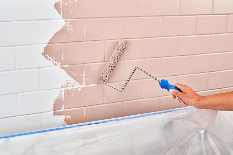 Applying paint to a tile backsplash using a roller.