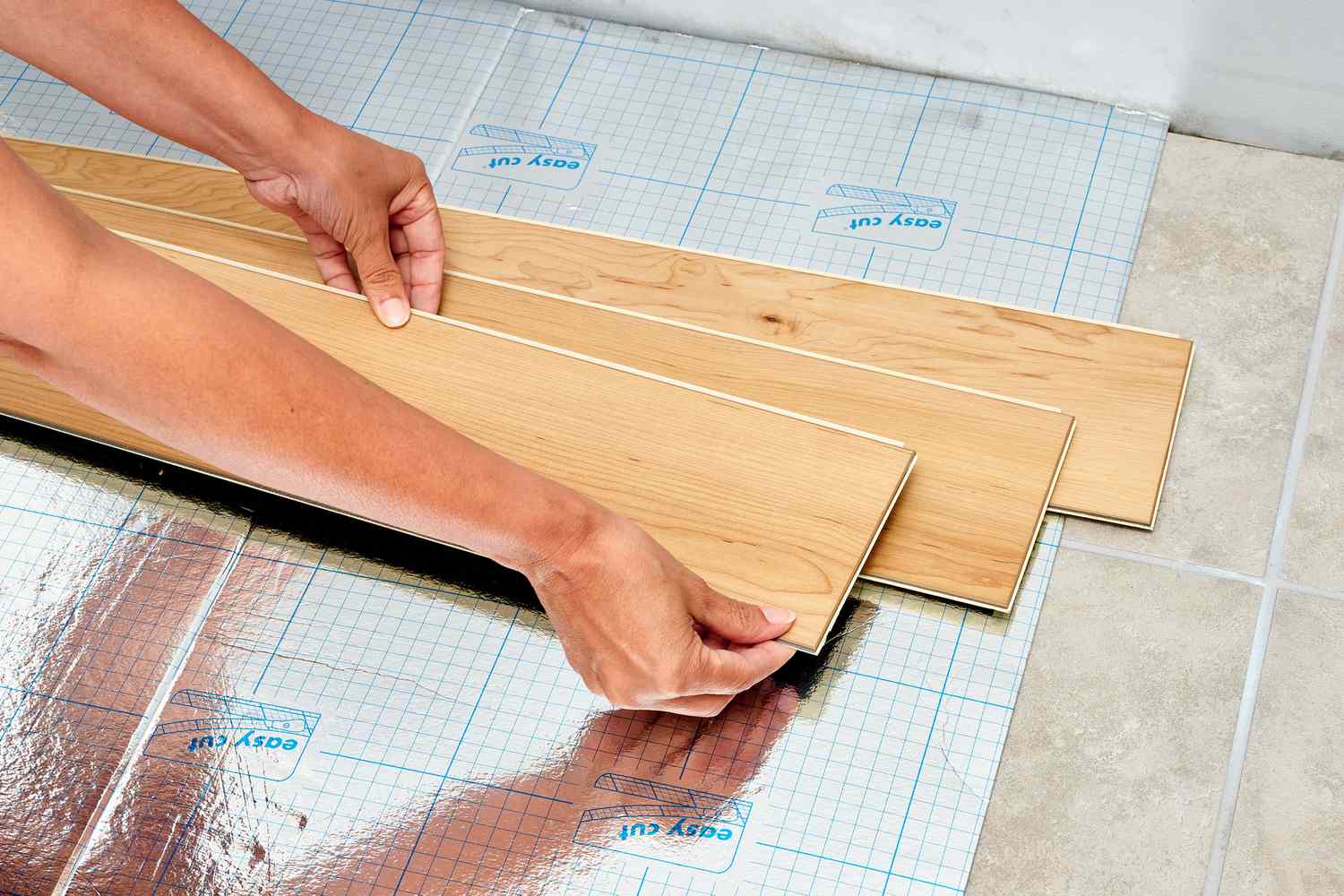 An individual installing vinyl flooring on the floor.