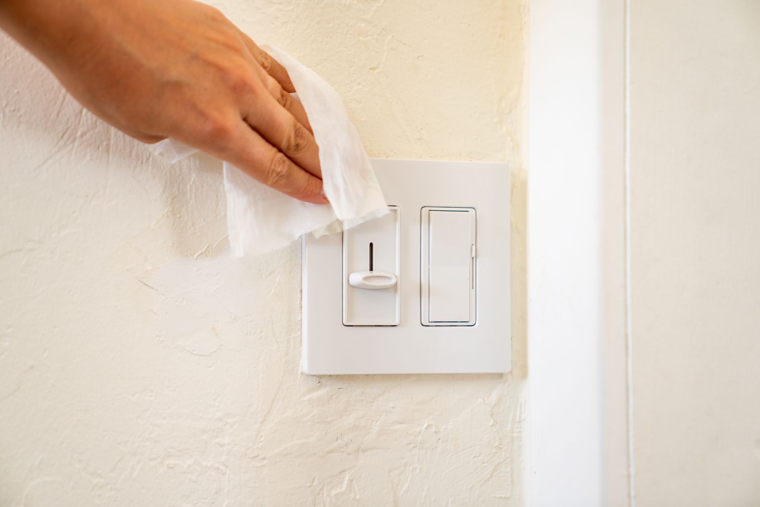 A disinfectant wipe is being used to clean the light switch as part of the weekly maintenance routine.