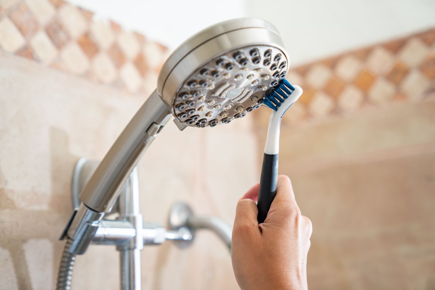 An old toothbrush is being used to clean the showerhead and eliminate soap scum.