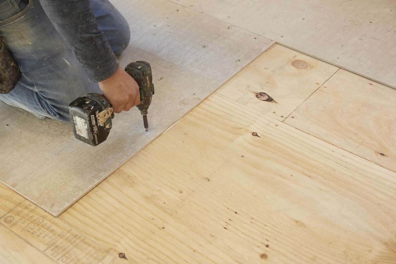 Cement backer boards manually fastened to a plywood floor with screws.