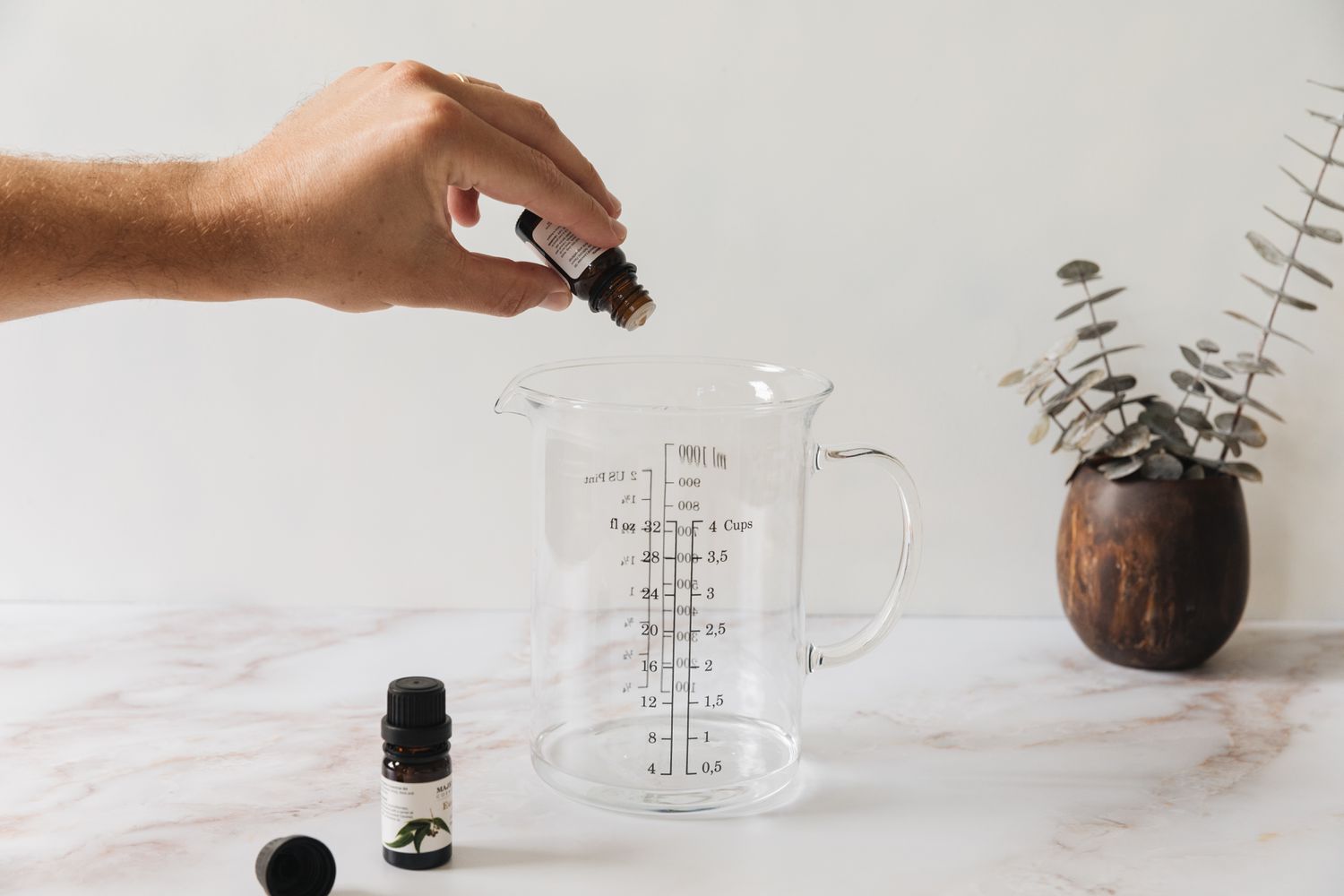 pouring essential oils into a measuring cup filled with vodka