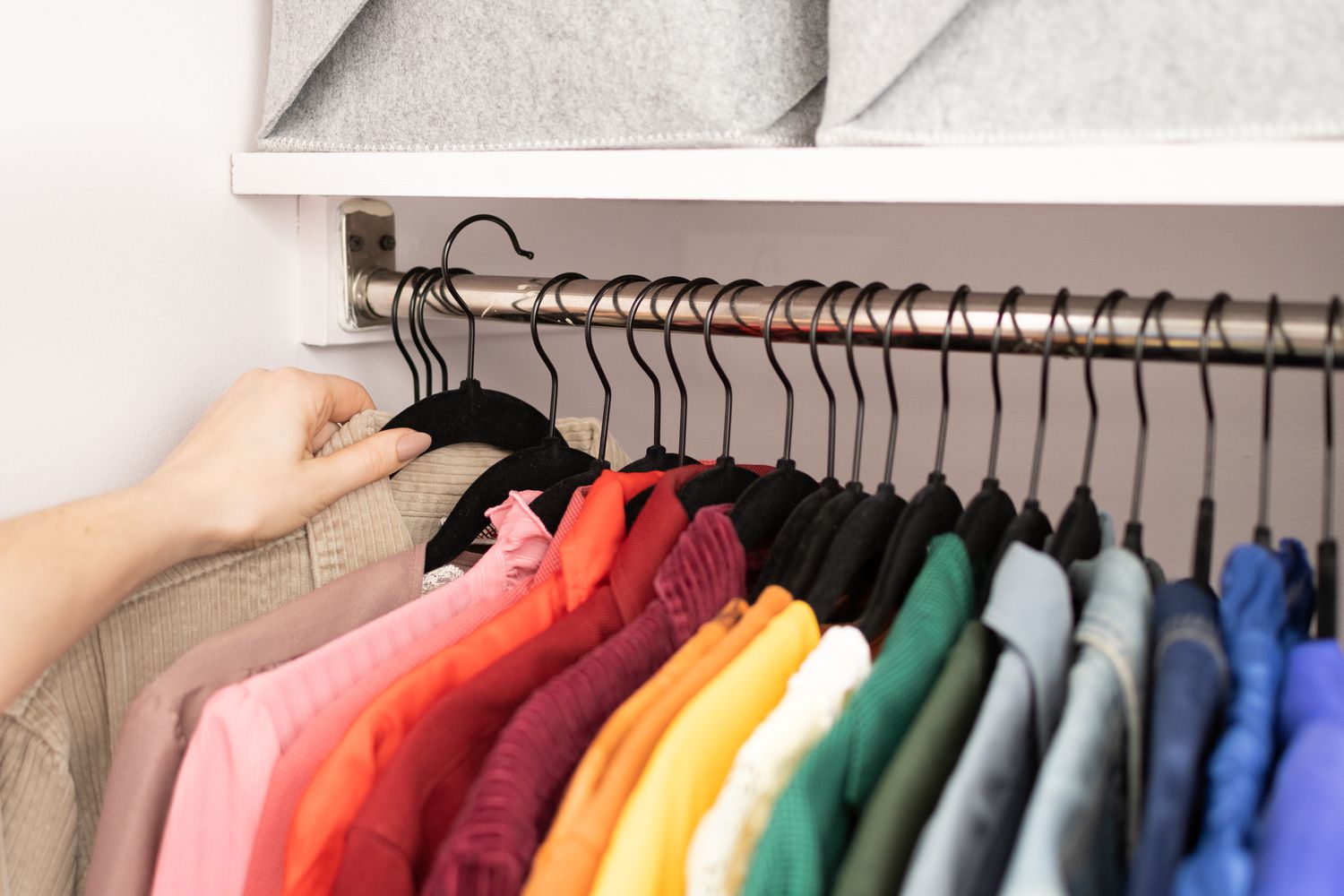 A neatly arranged closet with clothes organized by color on hangers.