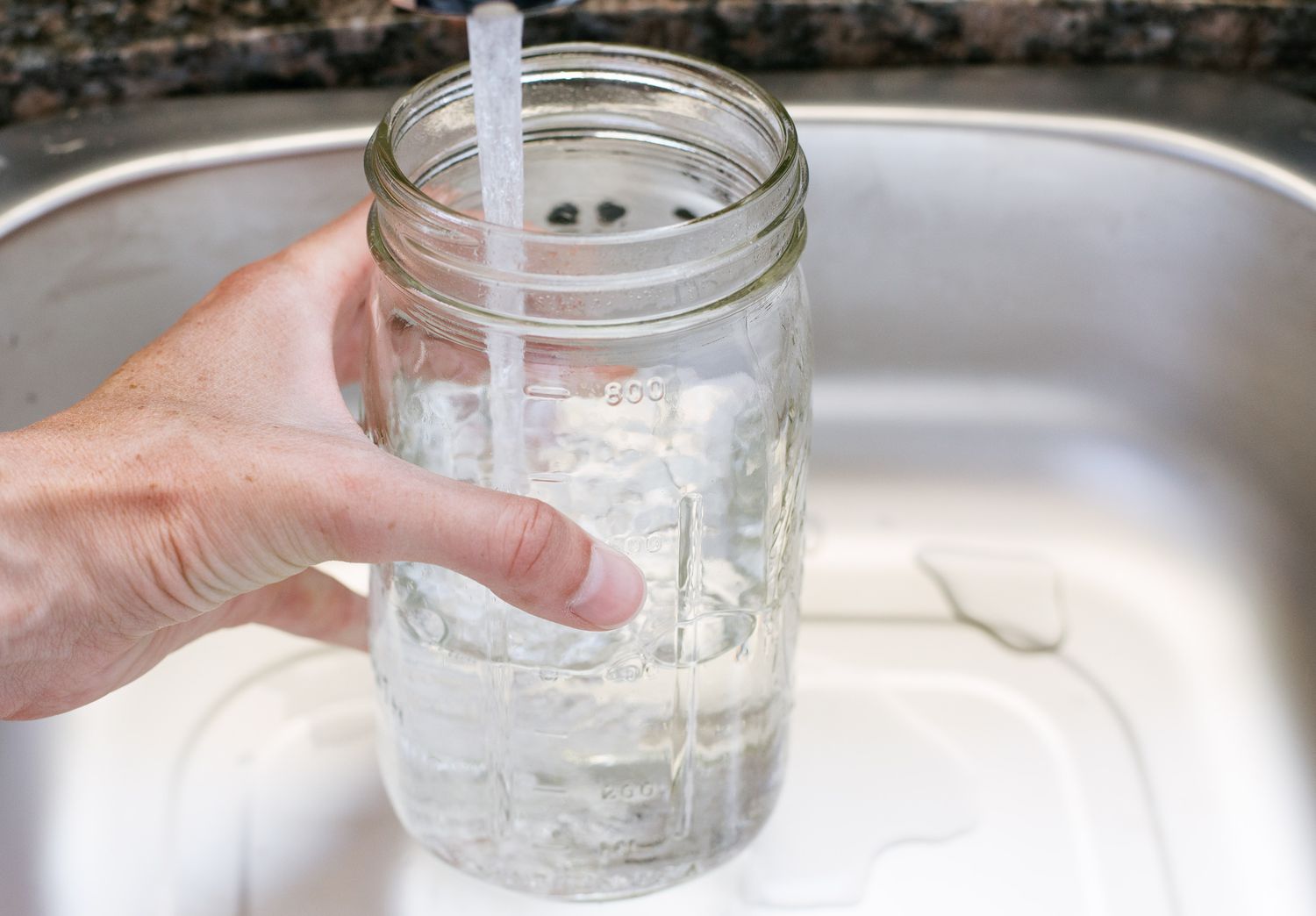 A glass container is being filled with water in the kitchen basin.