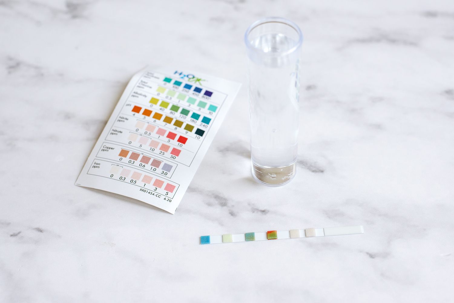 Test strip kit for assessing hard water, featuring colored indicators, positioned next to a glass container.