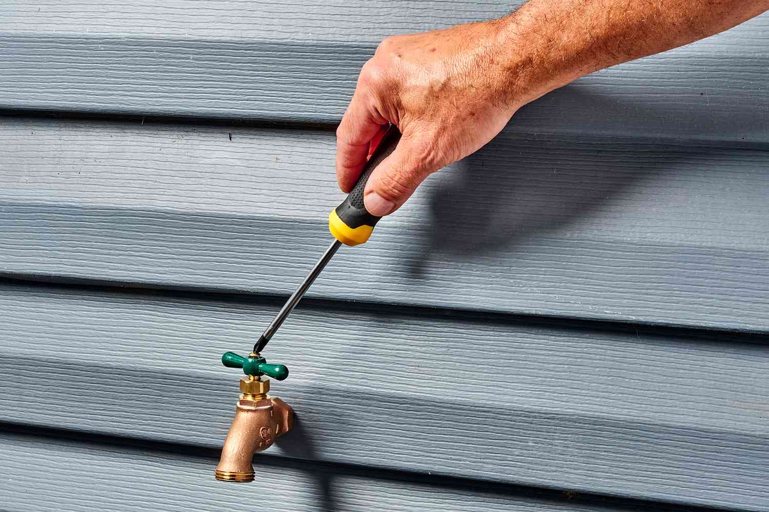 A screwdriver is being used to detach the green handle from the hose bib.