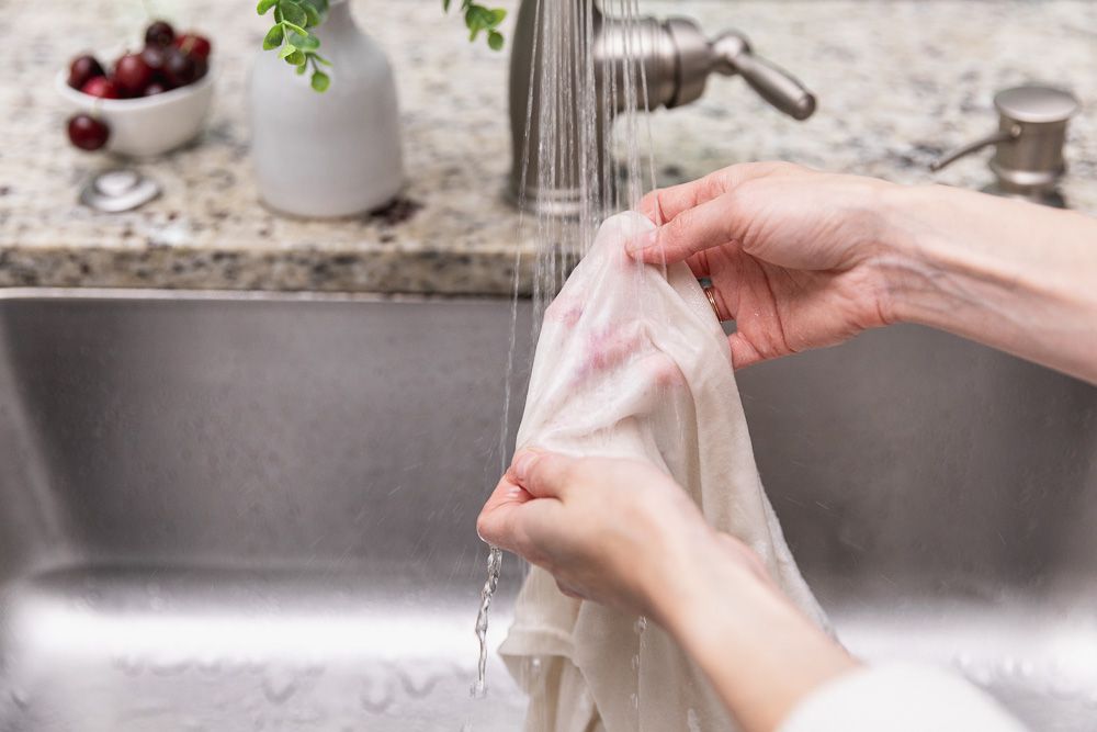 Cloth with cherry marks washed under a stream of water from the tap.