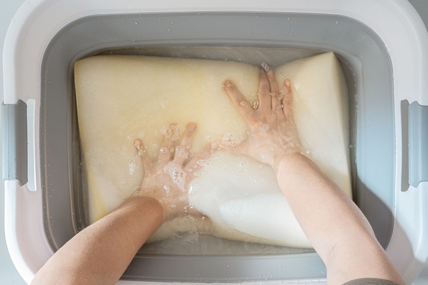 A memory foam pillow was placed in a tub filled with a mild detergent solution and water for the purpose of cleaning.